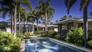Una piscina circondata da palme e vegetazione lussureggiante, con un edificio in pietra sullo sfondo.
