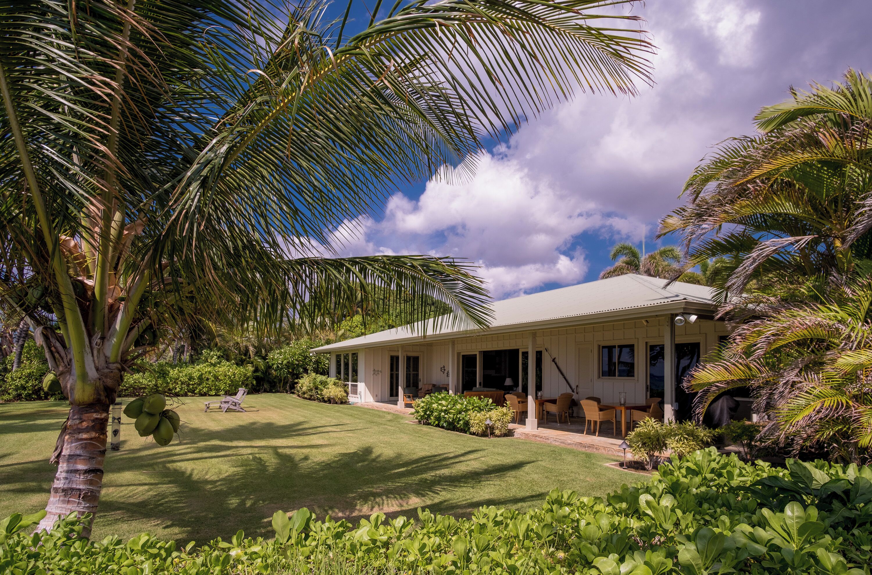 A house with a covered porch, a lawn, and palm trees.