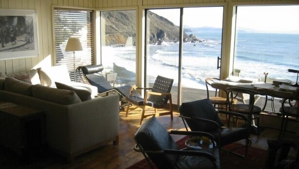 A living room with a view of the ocean, a sofa, chairs, and a table. - Ocean front property, minutes from San Francisco in the middle of National Park. (Muir Beach)