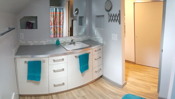 A modern bathroom with a curved vanity, a sink, and a mirror. There are towels hanging on the vanity, and a shower curtain is visible in the background. - Serene Loft for Outdoor Lovers  (Flagstaff)
