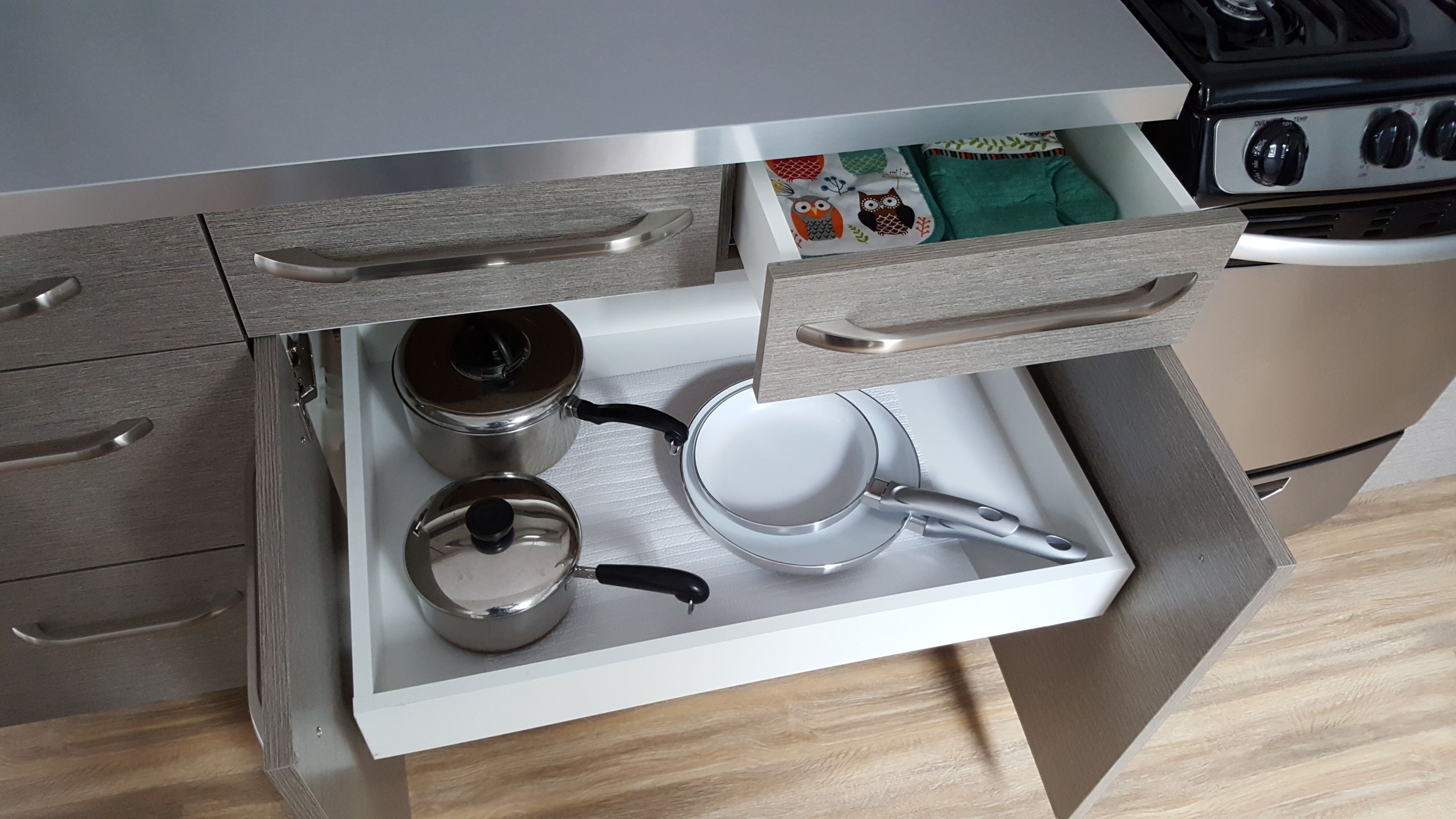 Un tiroir de cuisine contenant des ustensiles de cuisine en acier inoxydable, notamment une bouilloire, une casserole et une poêle.