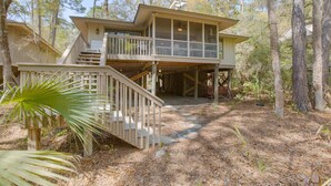 A two-story wooden house with a balcony and a covered patio area, surrounded by trees. - Inlet Cove Paradise #36 (Kiawah Island)