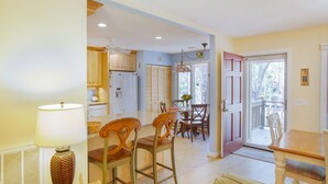 A spacious kitchen with wooden cabinets, a dining area with chairs, a table, and a view through a door to the outside. - Inlet Cove Paradise #36 (Kiawah Island)