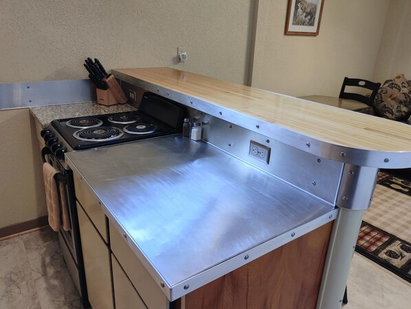 A kitchen with a stainless steel countertop, a stove, and a wooden backsplash.