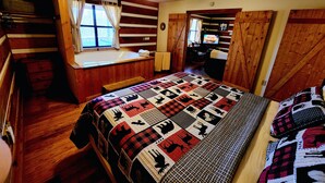 Een gezellig kamer in een chalet, met houten inrichting, een groot bed met sprei, een raam met gordijnen, een plafondventilator en een televisie.