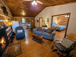 A cozy cabin interior with a fireplace, a sofa, a rocking chair, and a dining area.