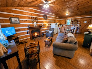 A cozy cabin interior with a fireplace, wooden walls, a television, and a dining area. - Maggie’s House Cabin: A Cozy Retreat with Mountain Views, Hot Tub, and Jacuzzi (Sieverville)