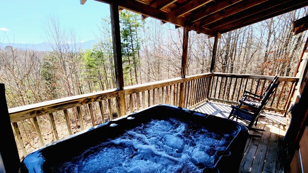 Een hottub op een houten terras met uitzicht op een bos en bergen.
