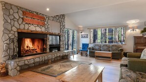 A cozy living room with a stone fireplace, a television, and comfortable seating. - Family friendly retreat, private forested acreage (Big Bear Lake)