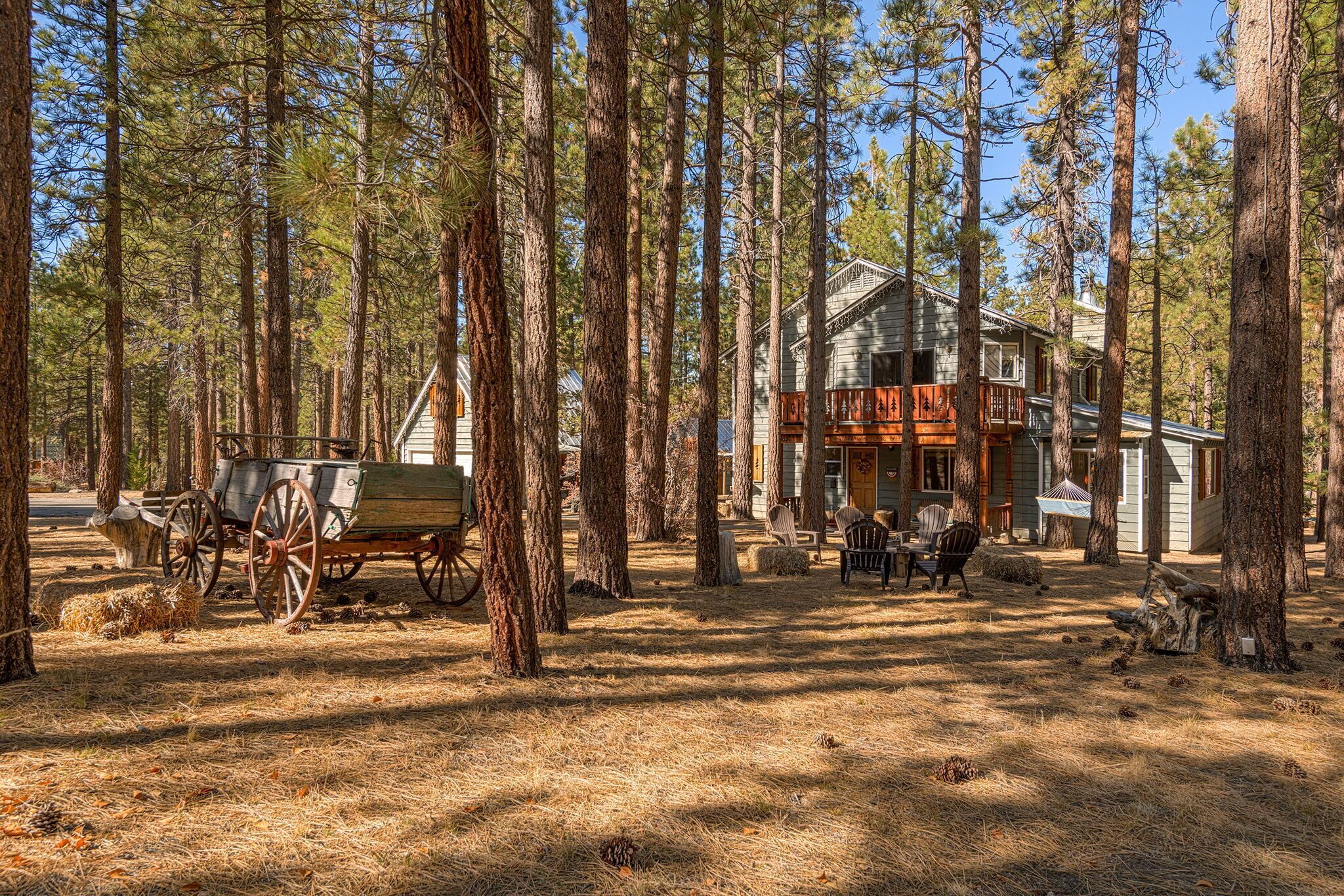 A cabin in a forest with a porch, a wooden cart, and a dining area.
