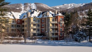 A multi-story hotel with balconies, snow-covered surroundings, and a mountainous backdrop.