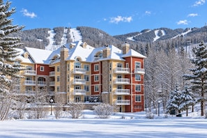 A multi-story hotel with balconies, set against a snowy mountain backdrop.