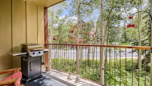 Un balcon avec un barbecue, une petite table et une vue sur une rue et des arbres.