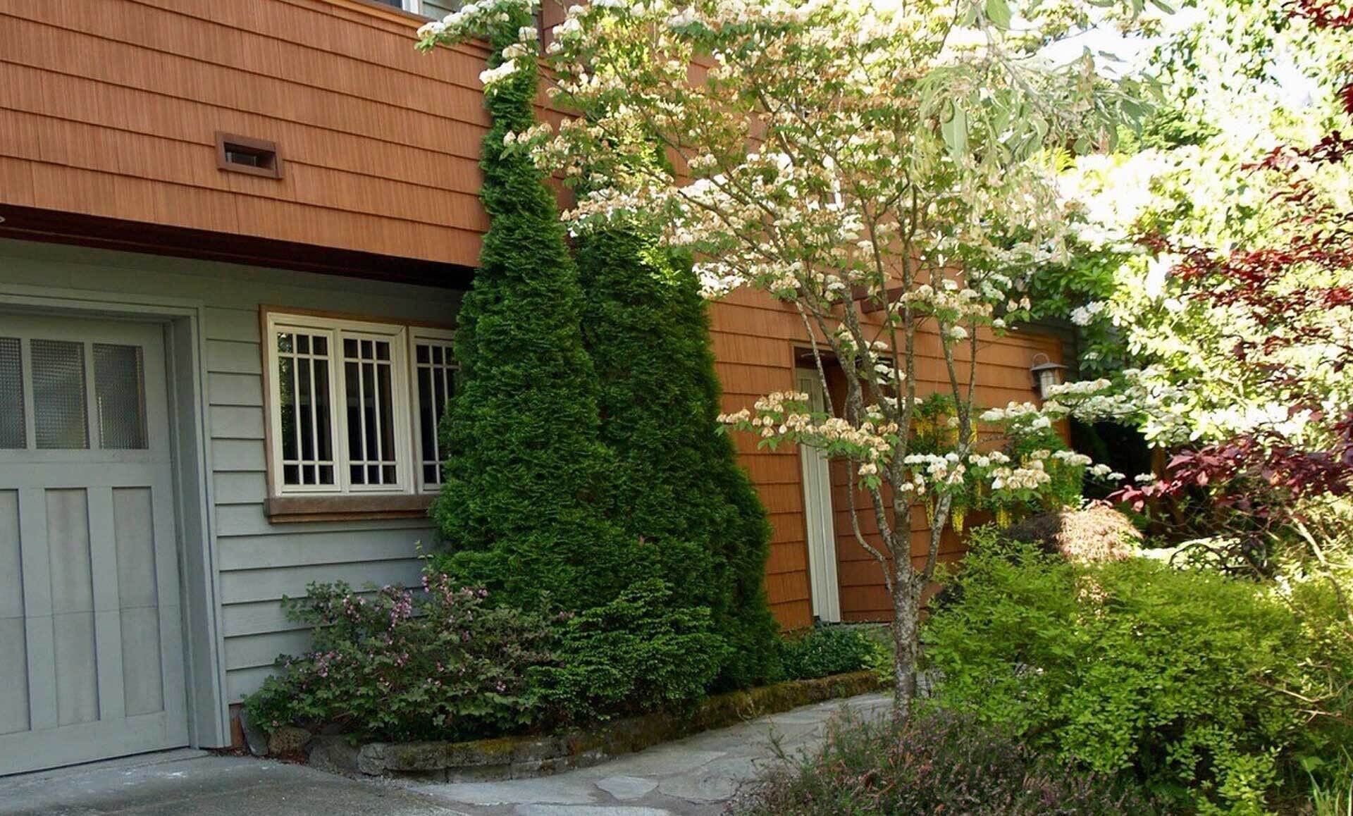 A residential building with a grey door, white-framed windows, and a wooden siding exterior.
