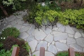 A stone patio with a glass table and metal chairs, surrounded by lush greenery. - Walking neighborhood minutes from downtown (Seattle)