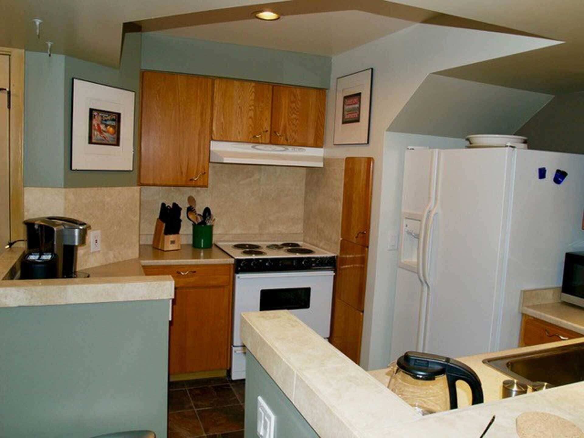 A compact kitchen with wooden cabinets, a stove, a refrigerator, and a coffee maker.