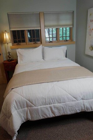 A neatly made bed with a quilted cover, a bedside lamp, and a window with blinds. - Walking neighborhood minutes from downtown (Seattle)