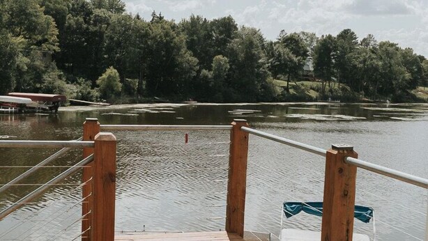 Une terrasse en bois avec une balustrade donnant sur un lac, entourée d’arbres.