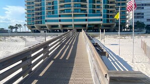 A beachfront hotel with a curved facade, multiple balconies, and a wooden boardwalk leading to the beach. - Sunny paradise! Beachfront, bay views & all the amenities! Welcome families! (Orange Beach)