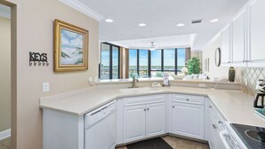 A modern kitchen with white cabinets, a large window with a view, and a ceiling fan. - Sunny paradise! Beachfront, bay views & all the amenities! Welcome families! (Orange Beach)