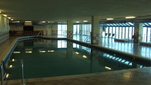An indoor swimming pool with clear glass walls, tiled floor, and a few chairs around the pool area. - Sunny paradise! Beachfront, bay views & all the amenities! Welcome families! (Orange Beach)