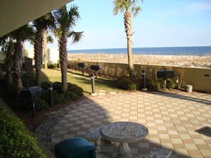 Eine Terrasse mit Fliesenboden, einem runden Tisch und zwei Stühlen. Palmen und Blick auf den Strand sind zu sehen.