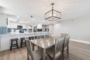 Une cuisine moderne avec des meubles blancs, un îlot central et un coin repas comprenant une table et des chaises en bois.