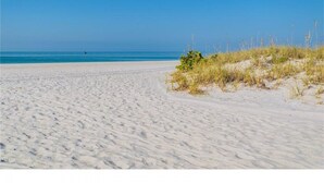 En sandstrand med klart, blått vatten och en person i fjärran.
