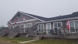 A two-story building with a grey exterior and white trim, featuring a set of wooden stairs leading to a porch area.
