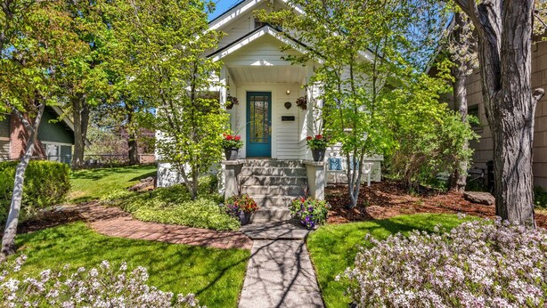 A two-story house with a front porch, a blue door, and a small garden with various plants and flowers. - Bluebird Day - Jefferson Cottage Cozy two-bedroom, perfect for family getaways. (Bend)