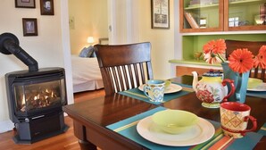A cozy room with a wood-burning stove, a dining table set with plates and a vase of flowers, and a bed in the background. - Bluebird Day - Jefferson Cottage Cozy two-bedroom, perfect for family getaways. (Bend)