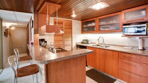 Uma cozinha moderna com armários de madeira, bancada de granito, micro-ondas embutido e um espaço de bar com banquetas.