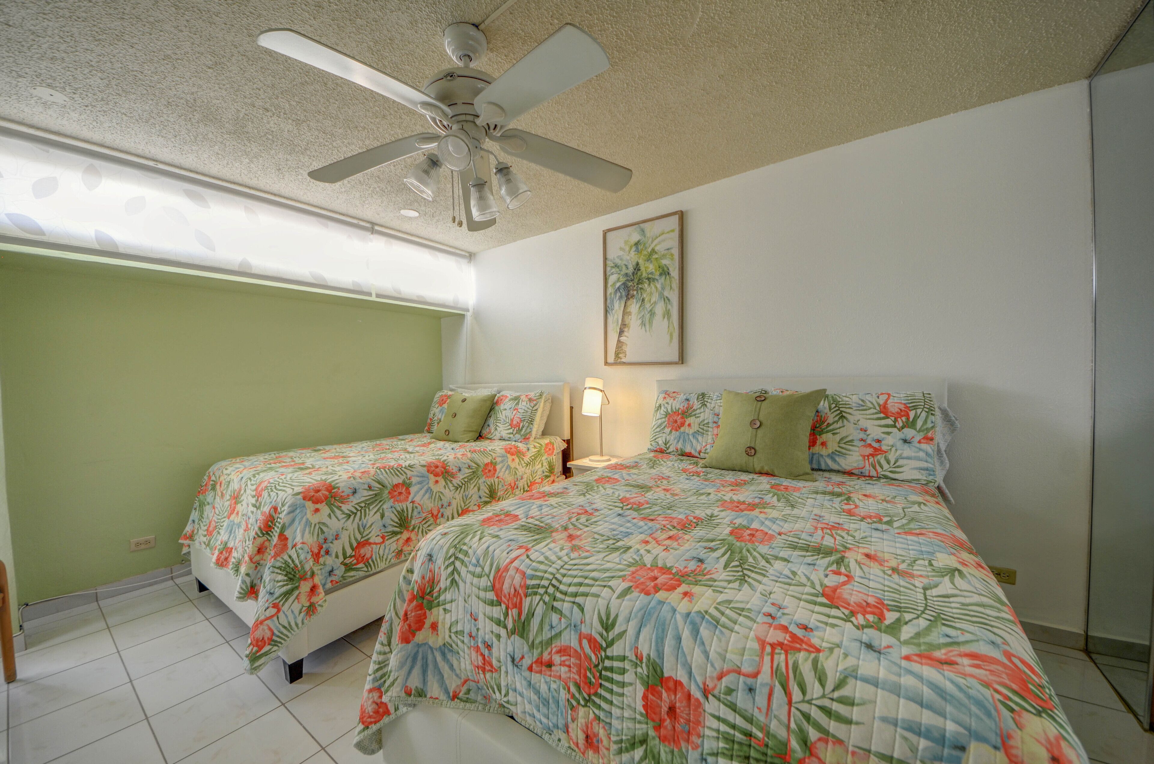 A bedroom with two beds, a ceiling fan, and a painting on the wall.