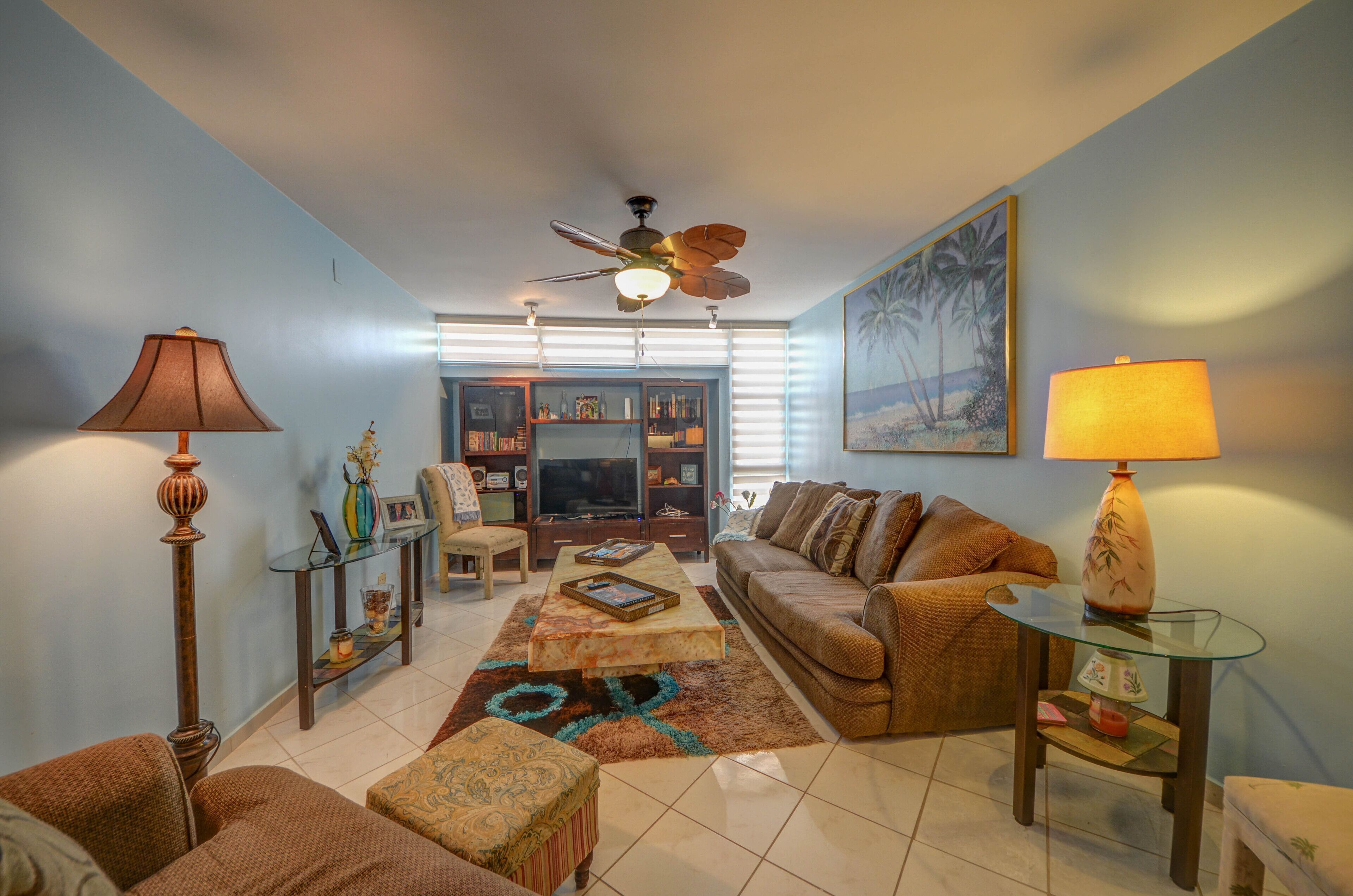 A living room with a sofa, armchairs, a coffee table, a TV, and a ceiling fan.