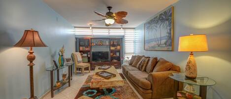A living room with a sofa, armchairs, a coffee table, a TV, and a ceiling fan.