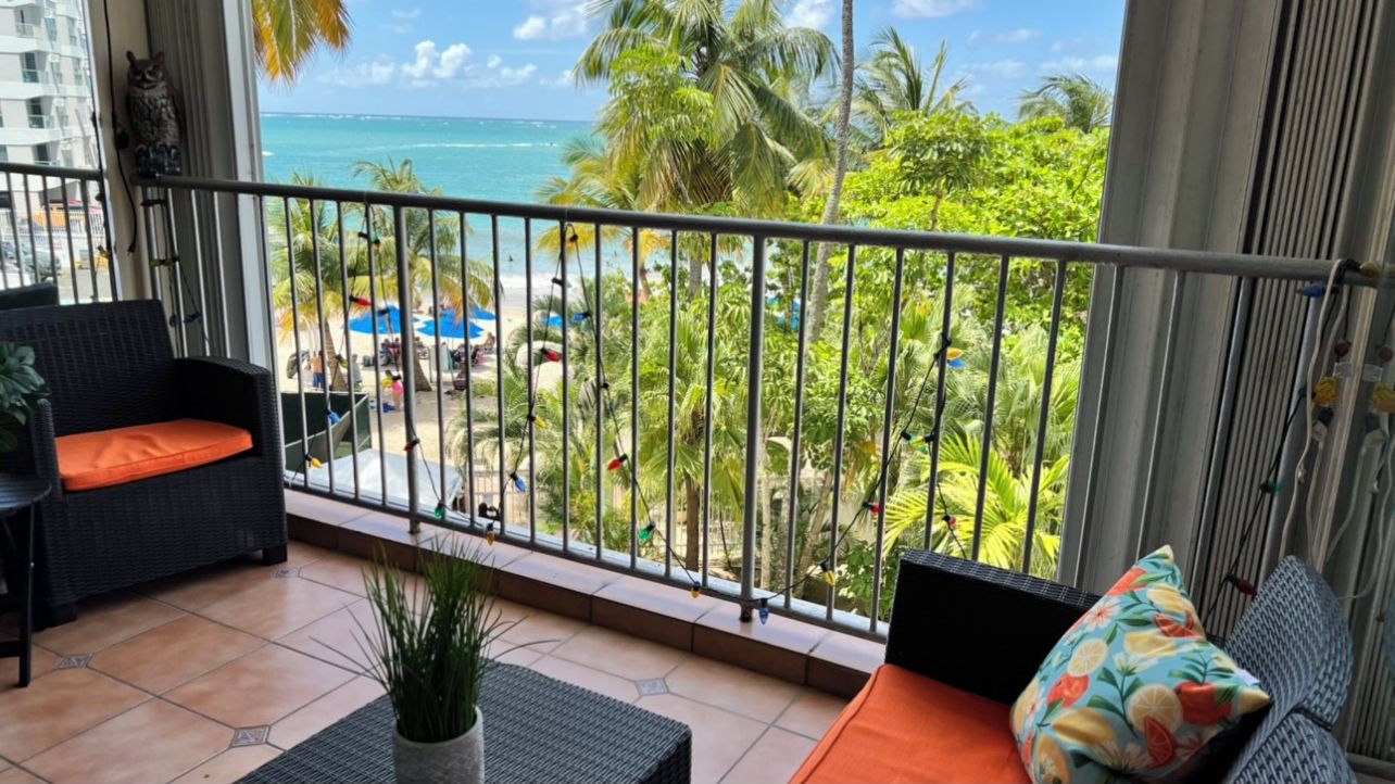 Ein Balkon mit Blick auf das Meer, ein Korbsessel, ein kleiner Tisch und ein Blumentopf.