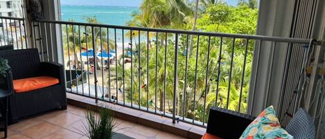 Ein Balkon mit Blick auf das Meer, ein Korbsessel, ein kleiner Tisch und ein Blumentopf.