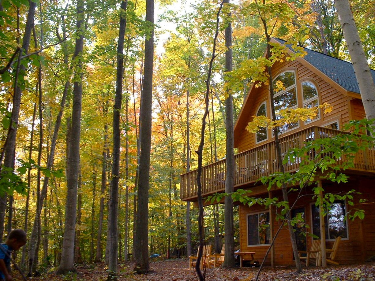 Une cabane en bois dotée d’un balcon, entourée de grands arbres aux couleurs automnales.