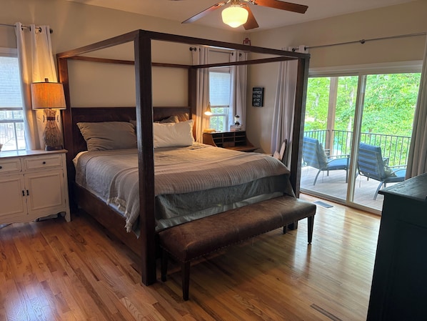 A four-poster bed with a bench, wooden flooring, a ceiling fan, and a view of the outdoors.