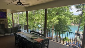 A covered outdoor dining area with a table and chairs, a stone fireplace, and a view of a lake with boats. - Dujardins waterfront lake Keowee home, with double dock on a deep, wide cove... (West Union)