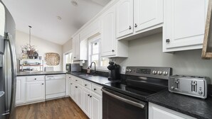 A modern kitchen with white cabinets, a black countertop, and stainless steel appliances including a refrigerator, dishwasher, oven, and toaster. - Dujardins waterfront lake Keowee home, with double dock on a deep, wide cove... (West Union)
