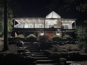 A two-story house with a balcony, a staircase leading to the entrance, and a well-maintained garden with rocks and shrubs.