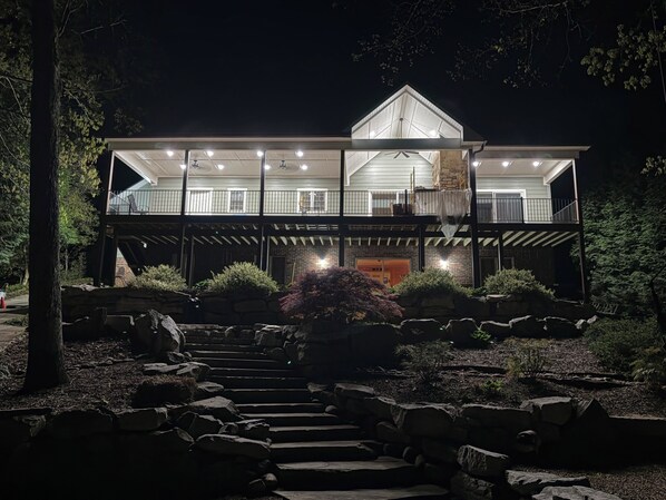 A two-story house with a balcony, a staircase leading to the entrance, and a well-maintained garden with rocks and shrubs.