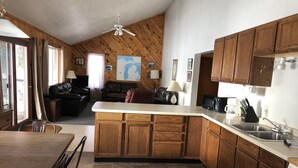 A kitchen with wooden cabinets, a dining area with a table and chairs, a sofa, and a ceiling fan. - Ride your sled from the front door! Ice fishing! Spacious & Clean with Parking! (AuTrain)