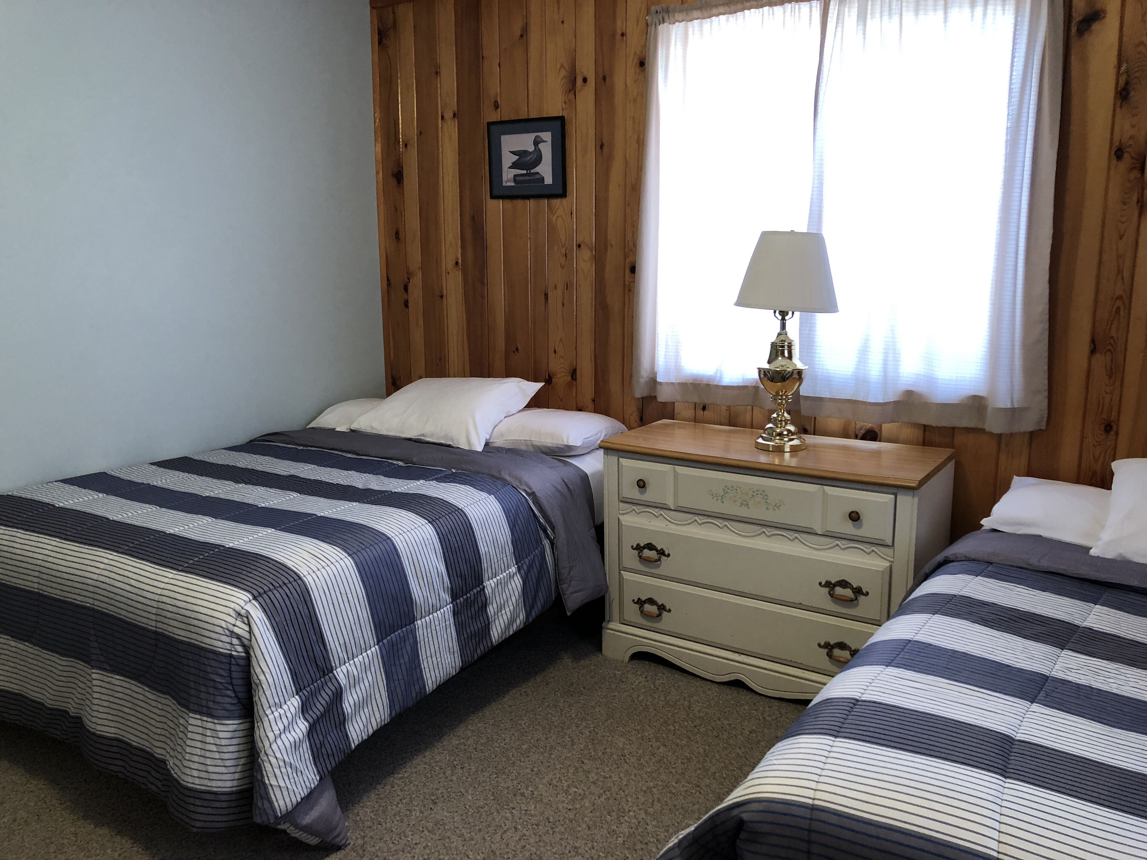 A bedroom with two beds, a wooden headboard, a nightstand with a lamp, and a framed picture on the wall.