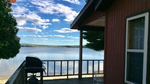 A wooden deck with a grill, a chair, and a view of a lake and distant hills. - Ride your sled from the front door! Ice fishing! Spacious & Clean with Parking! (AuTrain)