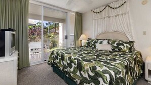 Un dormitorio con cama, ventilador de techo, televisión y puerta corrediza de vidrio que da a un espacio exterior.