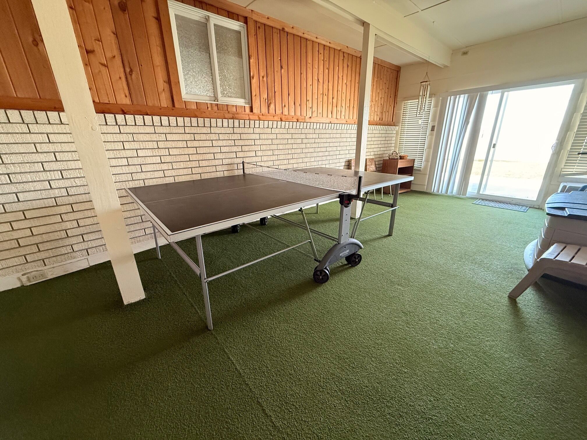 Una stanza con una moquette verde, un tavolo su ruote, un muro in mattoni, pannelli in legno e una finestra.