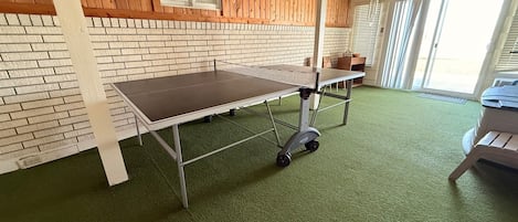 Una stanza con una moquette verde, un tavolo su ruote, un muro in mattoni, pannelli in legno e una finestra.