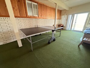 Een kamer met een groen tapijt, een tafel op wielen, een bakstenen muur, houten lambrisering en een raam.